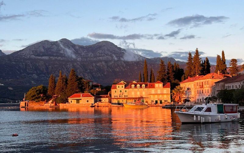 Вечерний вид на прибрежный город в Черногории с горами на заднем плане и лодкой в бухте.
