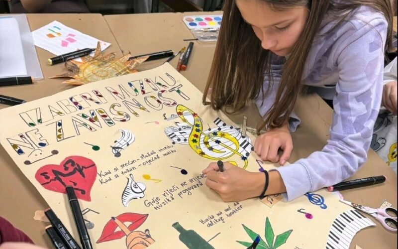 Ученики создают постер на школьном мероприятии в Черногории, рисуют музыкальные символы и надписи.
