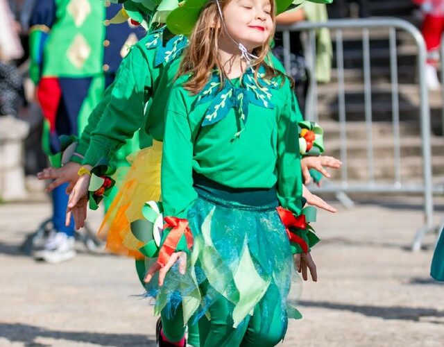 Маскарад на фестивале в Черногории: дети в ярких костюмах зеленого цвета празднуют на улице.