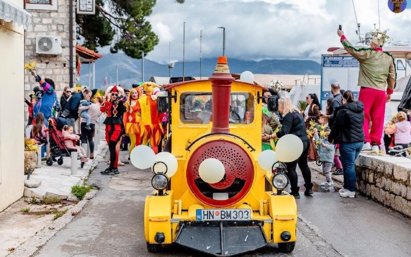 Парад в Черногории на улице с карнавальными костюмами и разноцветным поездом, люди наслаждаются праздником.