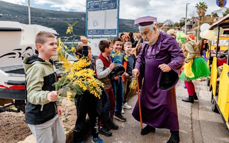 Карнавал в Черногории: дети дарят цветы артисту в костюме, праздник на улице весной.