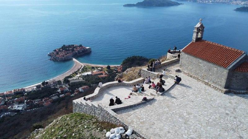 Изображение: вид на остров Святого Стефана в Черногории, посетители наслаждаются пейзажем с террасы над морем.