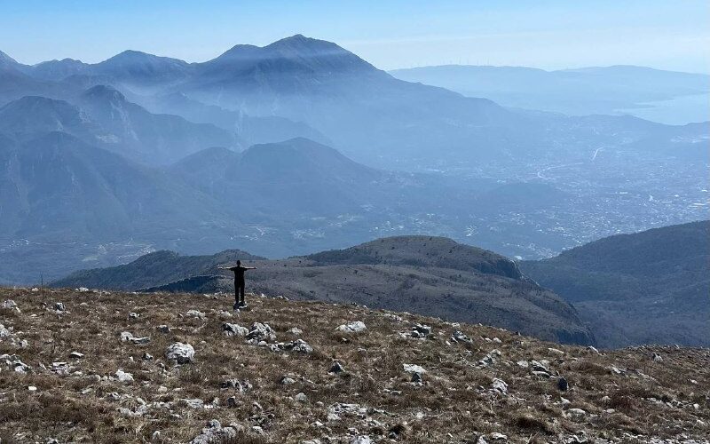 Человек стоит на вершине горы в Черногории, наслаждаясь видом на горы и долины.