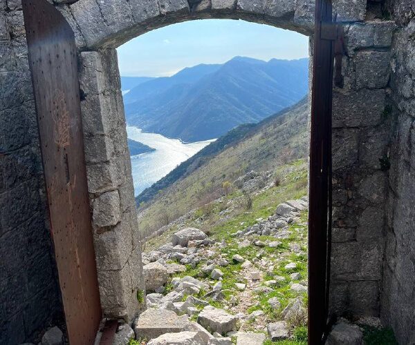 Вид на горы и залив через каменную арку в Черногории, популярное место для мероприятий и туризма.