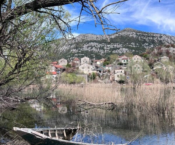 Старый деревянный лодка у тихого берега в Черногории, живописное село на фоне гор.