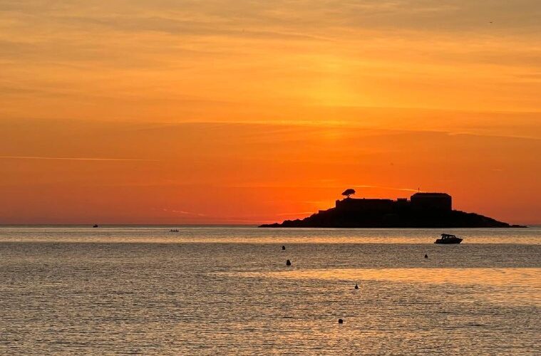 Закат на Адриатическом побережье Черногории, оранжевое небо и остров на фоне плавучих лодок.