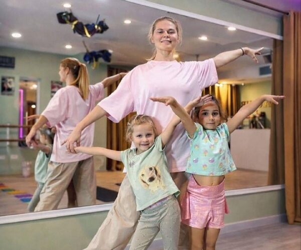 Дети и инструктор на занятии по танцам в Черногории, радостно позируют перед зеркалом в студии.