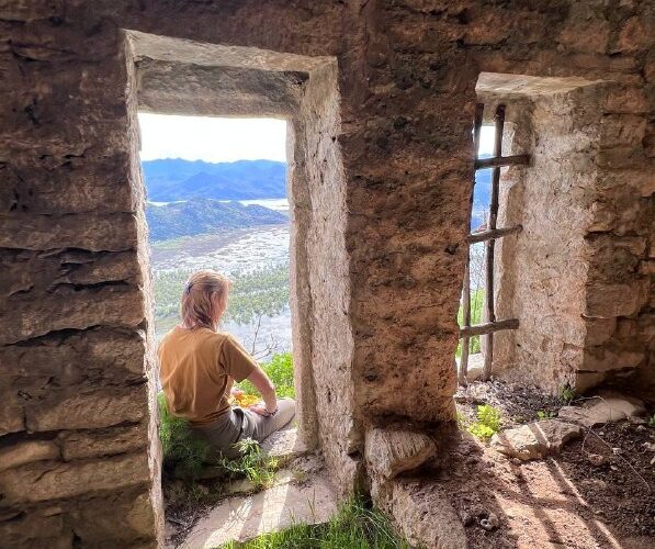Человек сидит в древних руинах в Черногории, любуясь живописными горами и долиной через оконный проем.